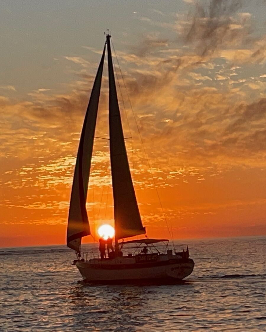 The Key Breeze under sail with the sun setting between its sails